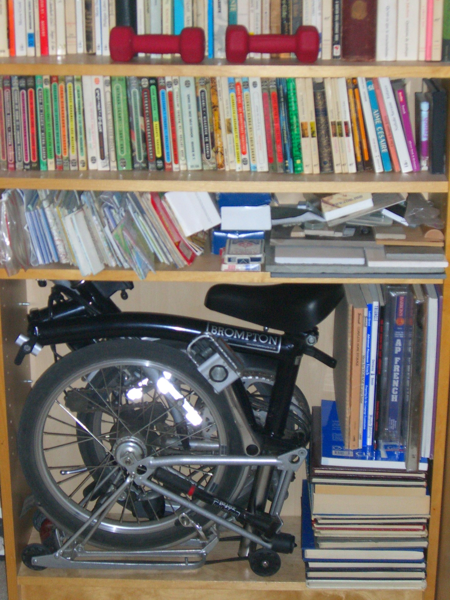 Fully folded black Brompton bicycle stored on a bookshelf
