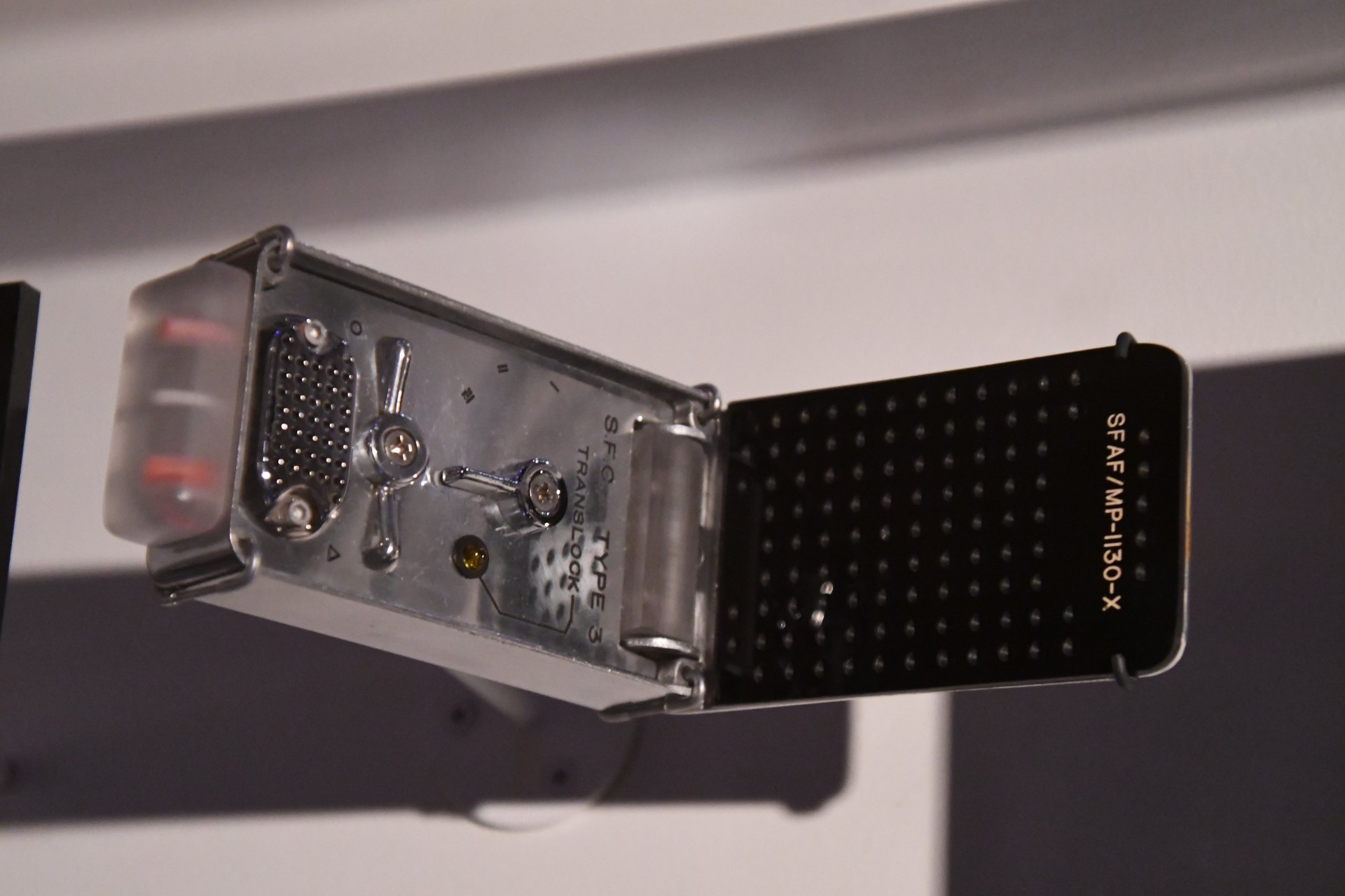 Original-series-style Star Trek communicator, flip lid open on a museum stand